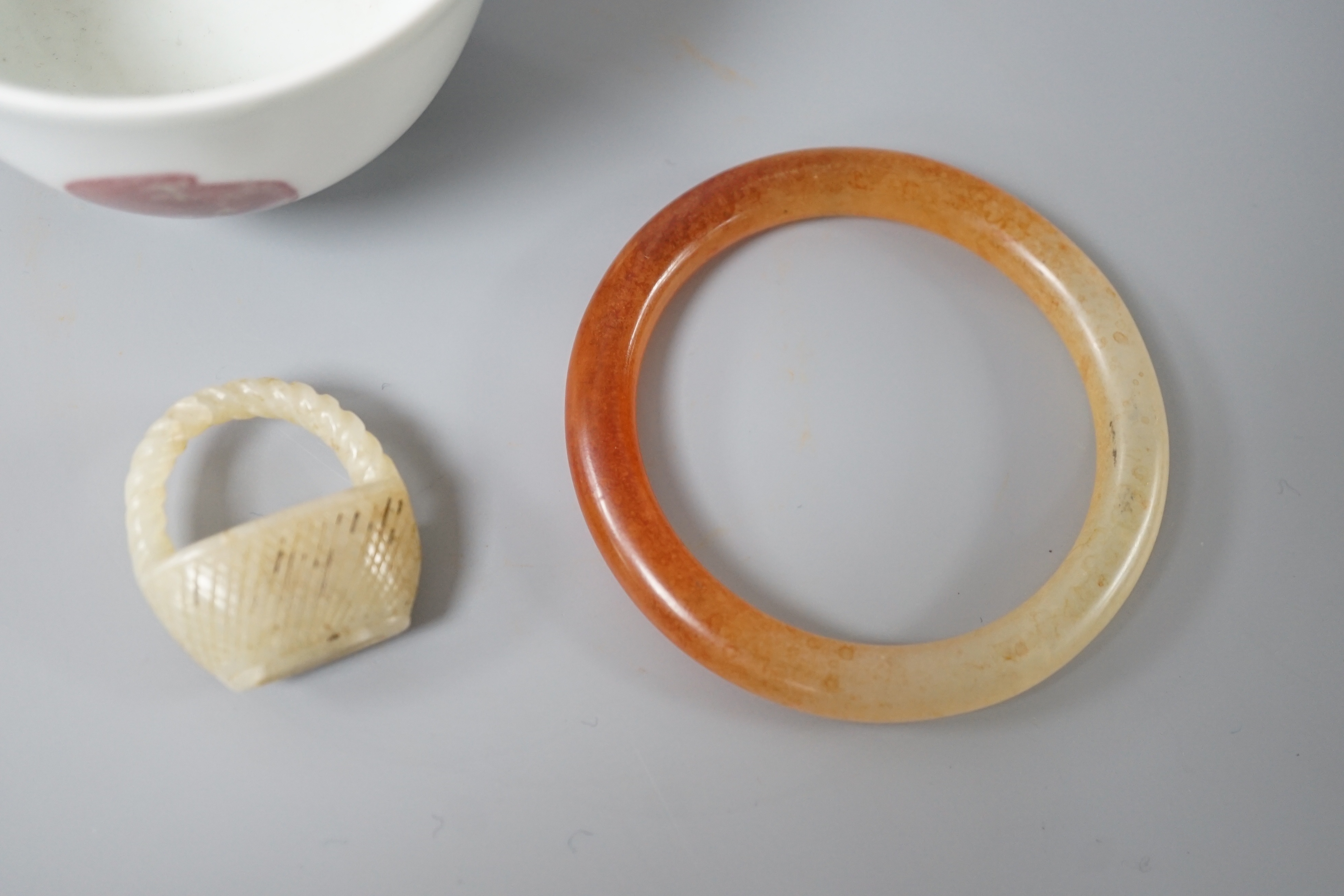 A Chinese porcelain teabowl with ‘fruit’ decoration, an agate bangle and a similar ‘basket’ carving.